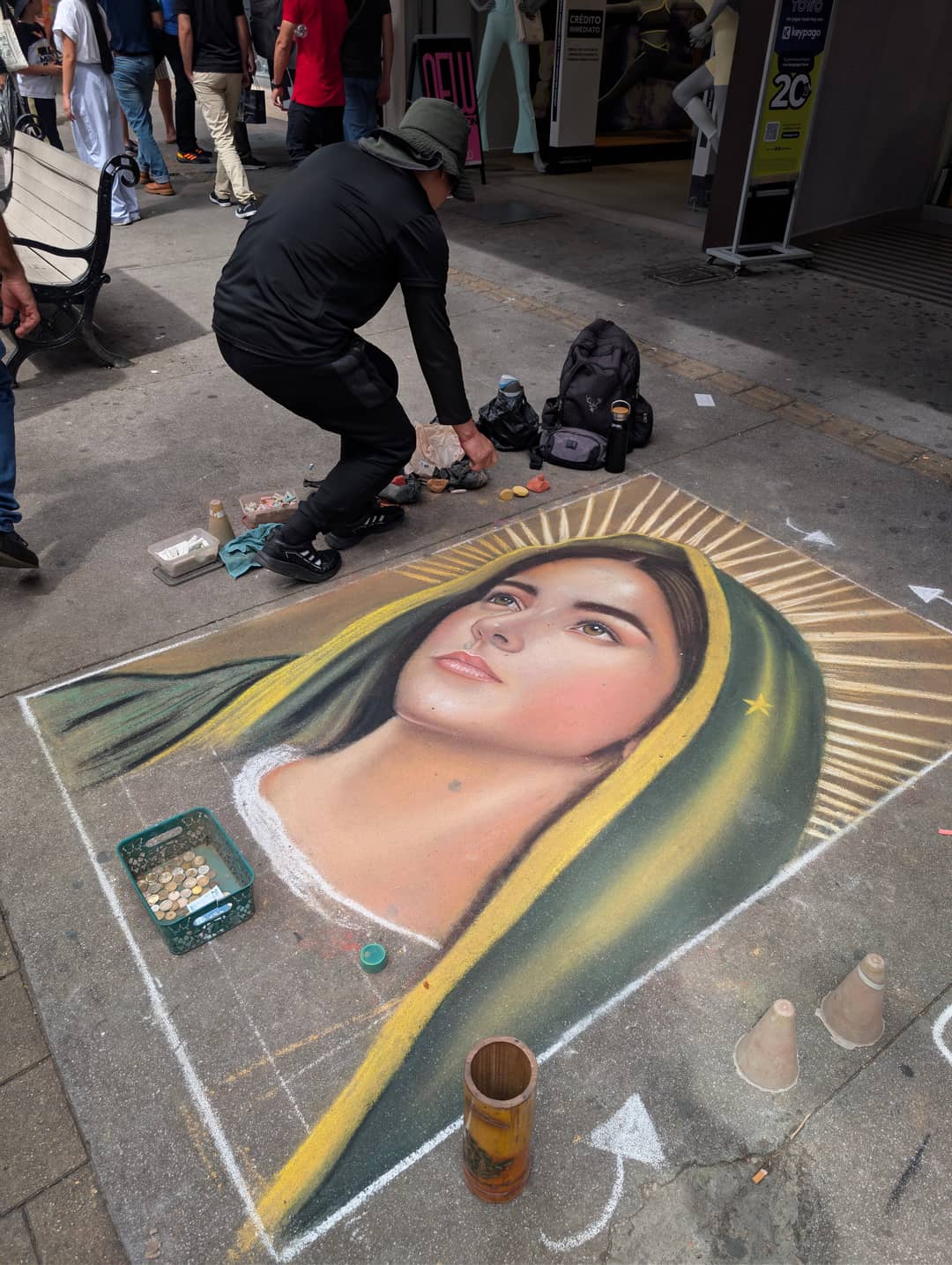 A man draws the Virgin of Guadalupe in pastel straight onto the paving. In an hour people will be walking over her.