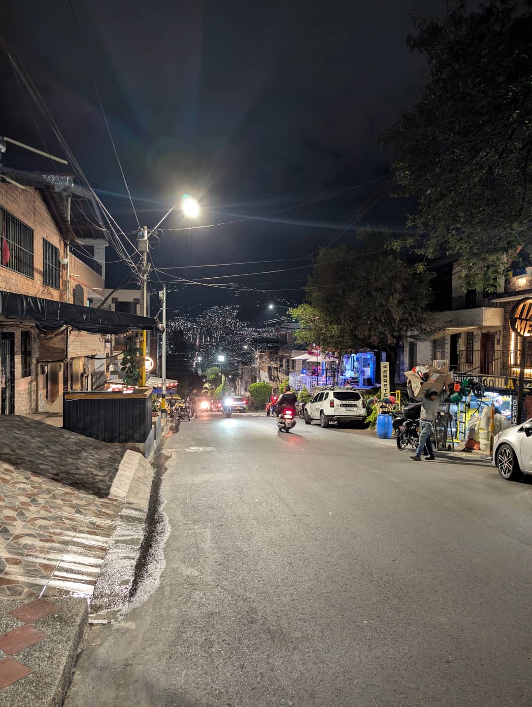 The street in the evening: people outside, bars open, motorbikes everywhere.