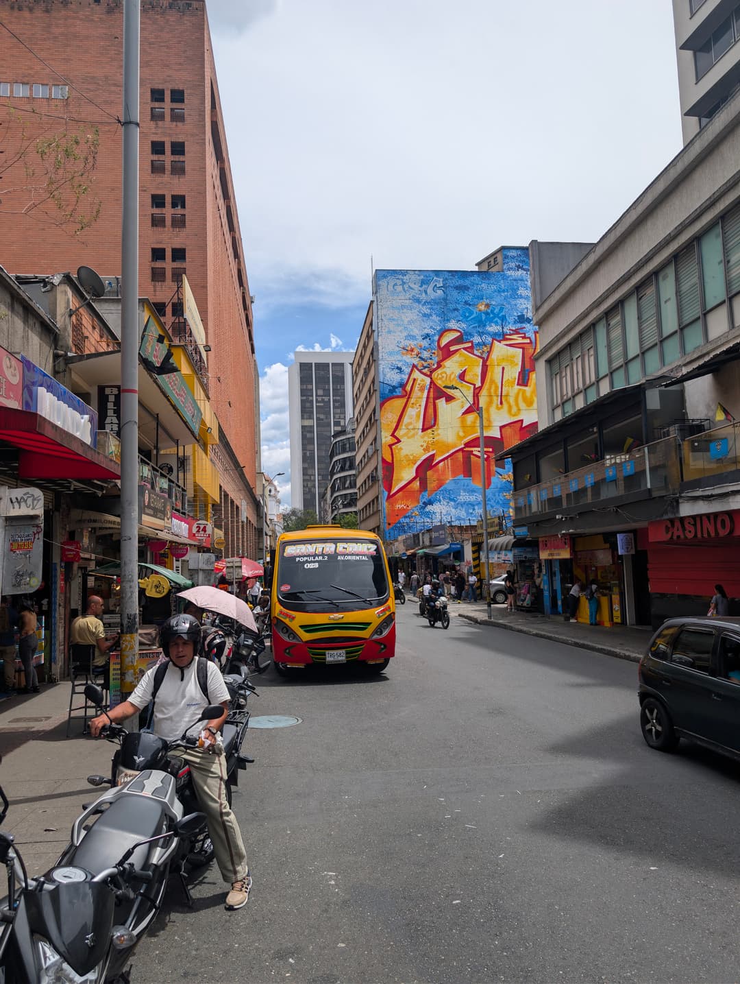 A street in the centre: a bus, motorbikes, stalls and people crossing anywhere.