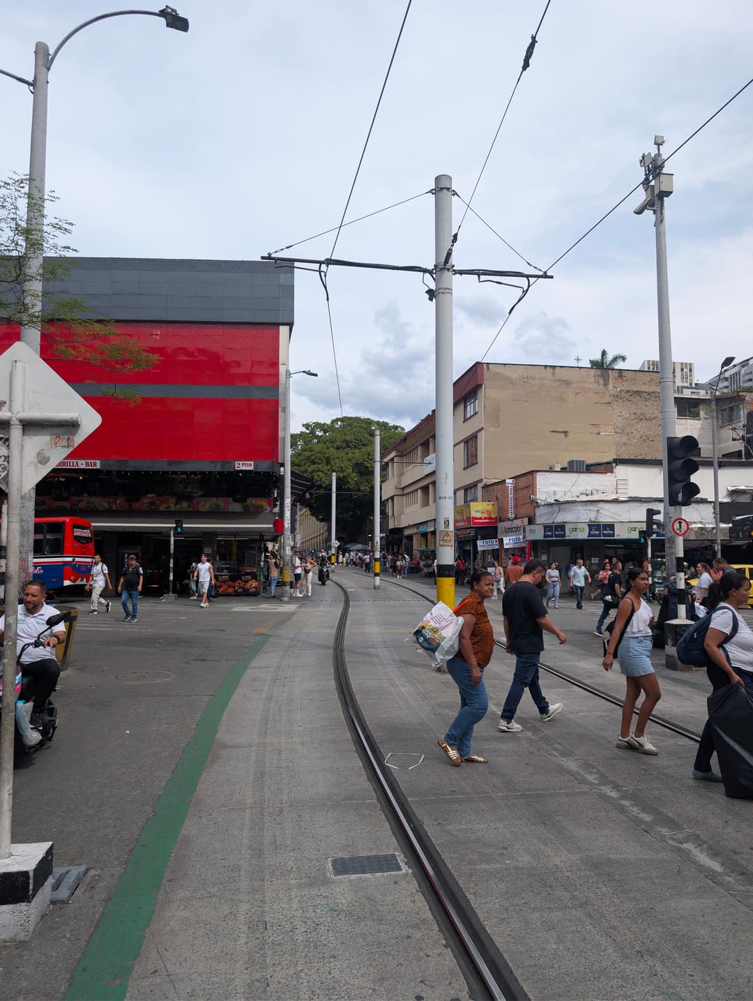 Ulice Ayacucho: tramvaj, obchody, motorky a lidi napříč kolejí.
